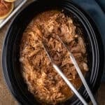 easy slow cooker pulled pork in a black crock pot with tongs