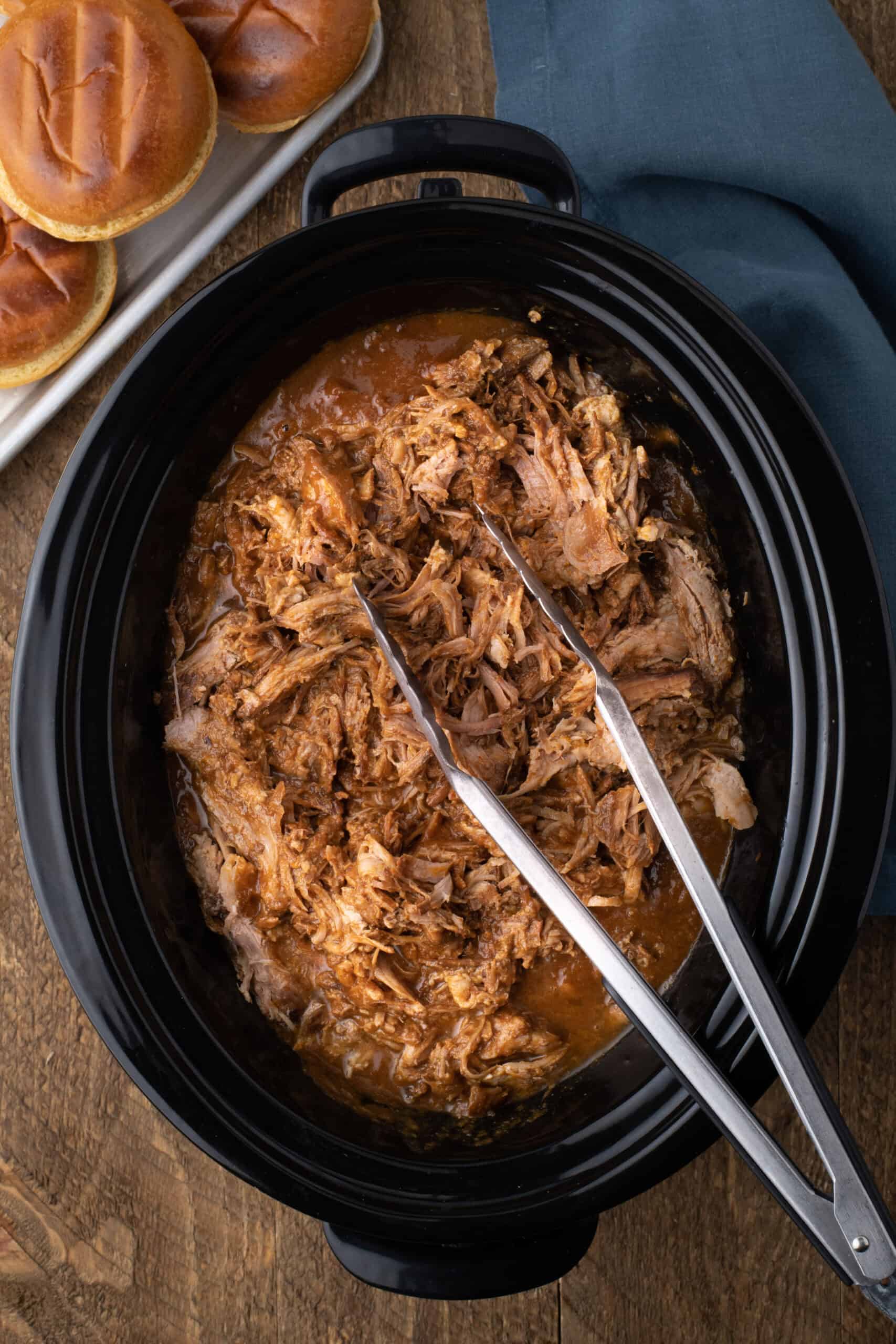 easy slow cooker pulled pork in a black crock pot with tongs