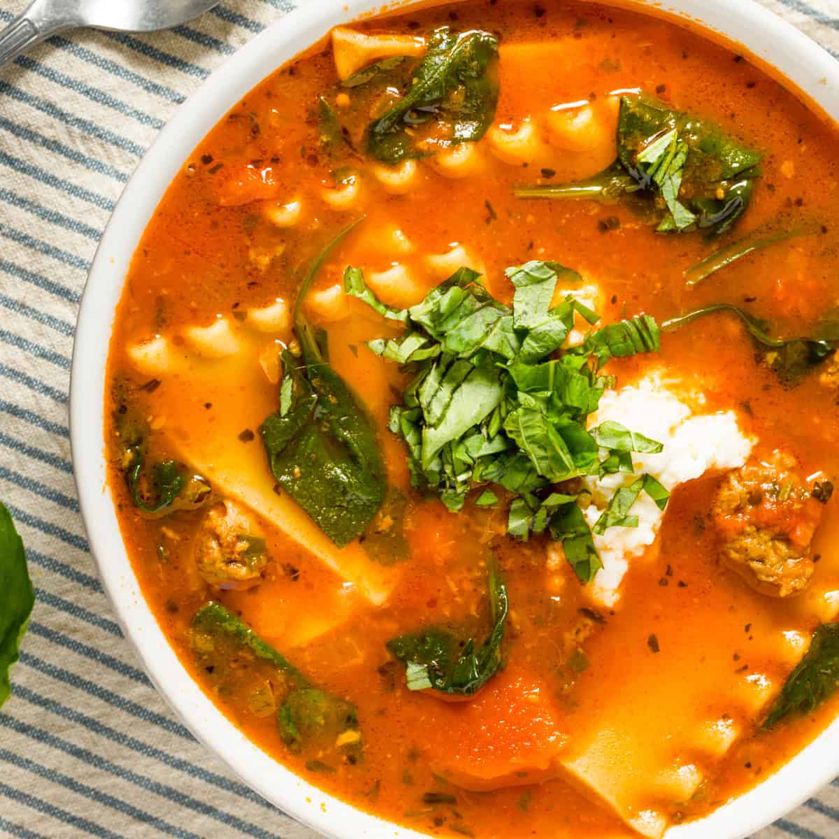 slow cooker lasagne soup in a white bowl with ricotta cheese and basil on top