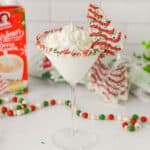 Christmas Tree Cake Martini in a glass with sprinkle frosted rin and a mini Christmas tree cake on the glass
