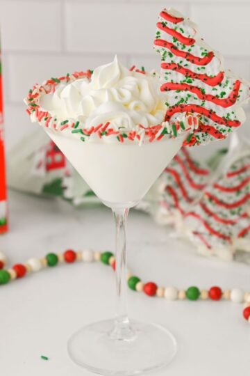 Christmas Tree Cake Martini in a glass with sprinkle frosted rin and a mini Christmas tree cake on the glass