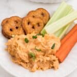 Crockpot Buffalo Chicken Dip on a white plate served with veggies and pretzels