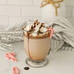 Crockpot Peppermint Hot Chocolate in a clear glass drizzled with chocolate and decorated with mini candy candes