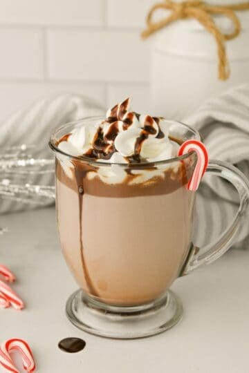 Crockpot Peppermint Hot Chocolate in a clear glass drizzled with chocolate and decorated with mini candy candes