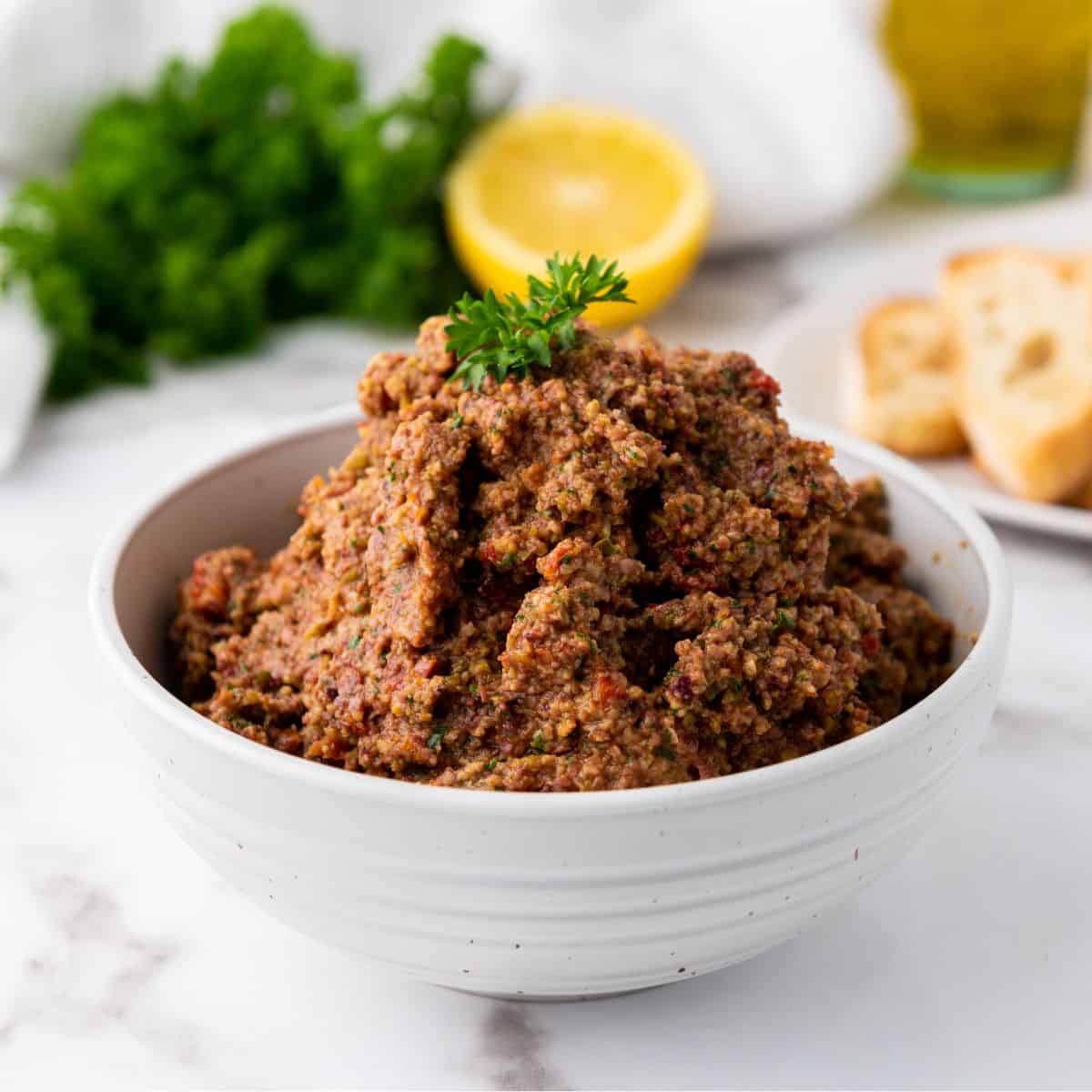 Homemade Olive Tapenade served in a white bowl on a marble counter