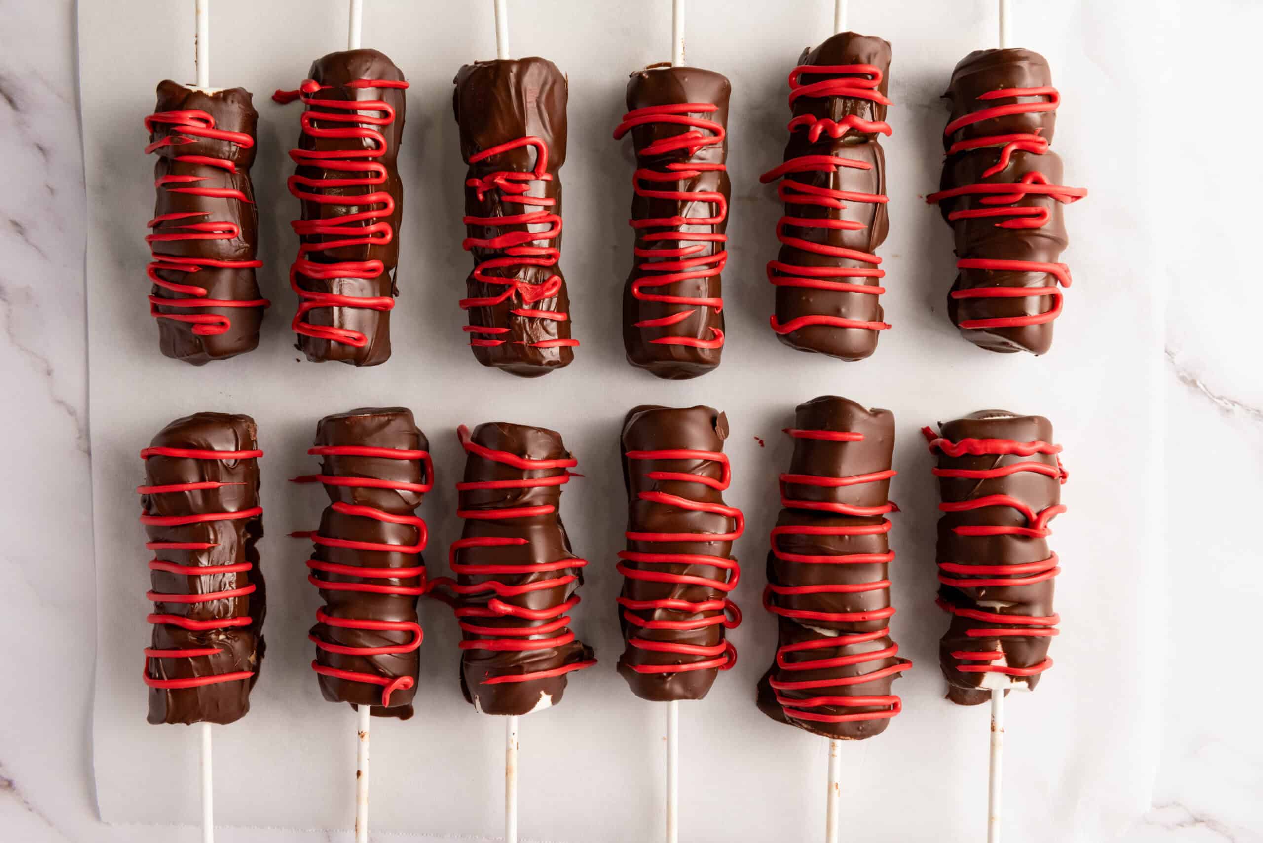 chocolate covered marshmallow pops being drizzled with red icing