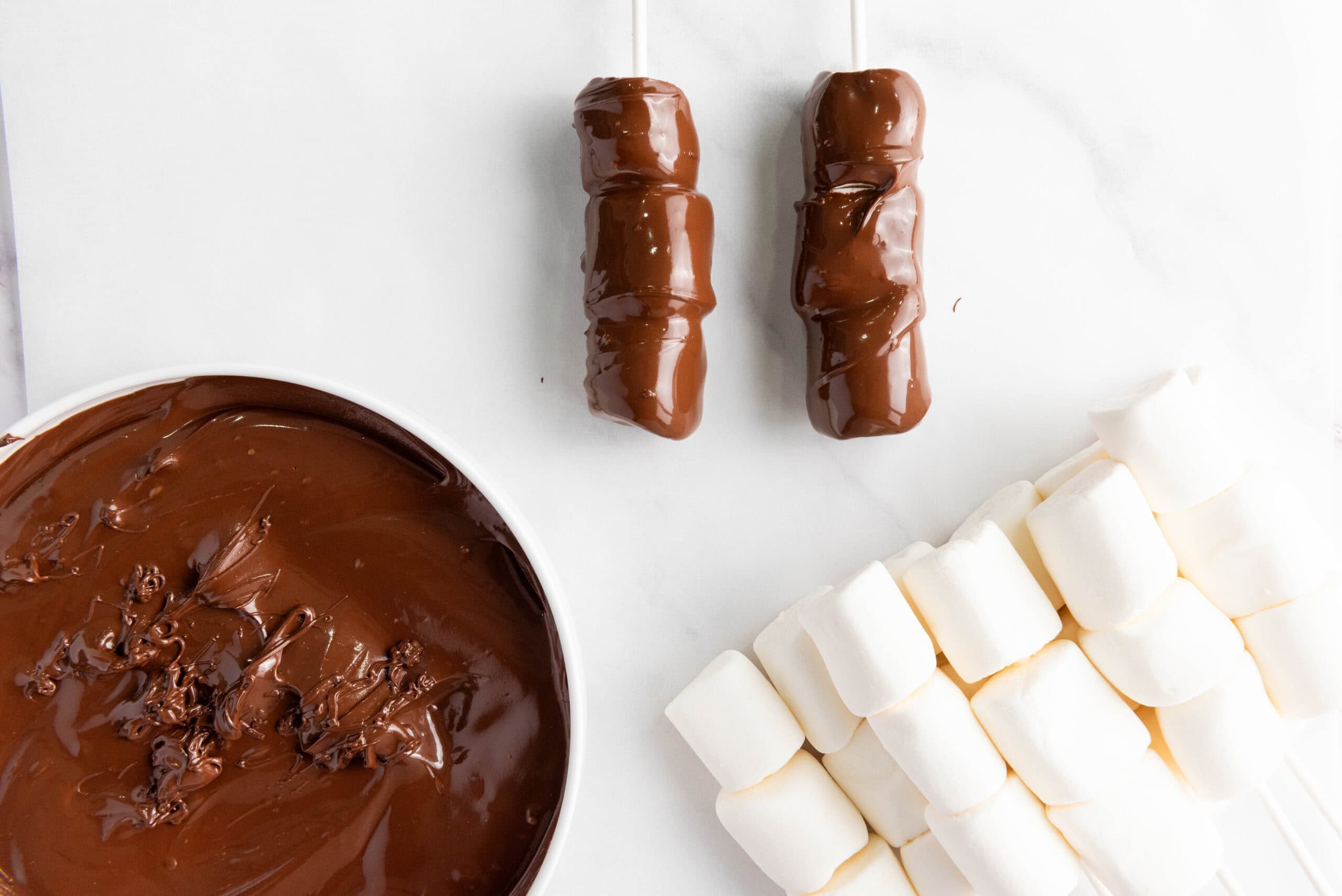 adding marshmallows to a lollipop stick and dipping them into melted chocolate