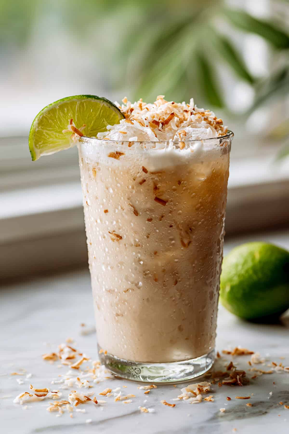 coconut lime dirty soda with dr pepper next to a window garnished with coconut shavings and a lime wedge