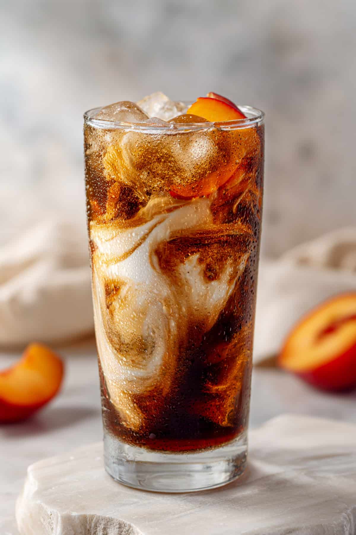 peach dirty soda with dr pepper on a light brown backdrop with peach slices