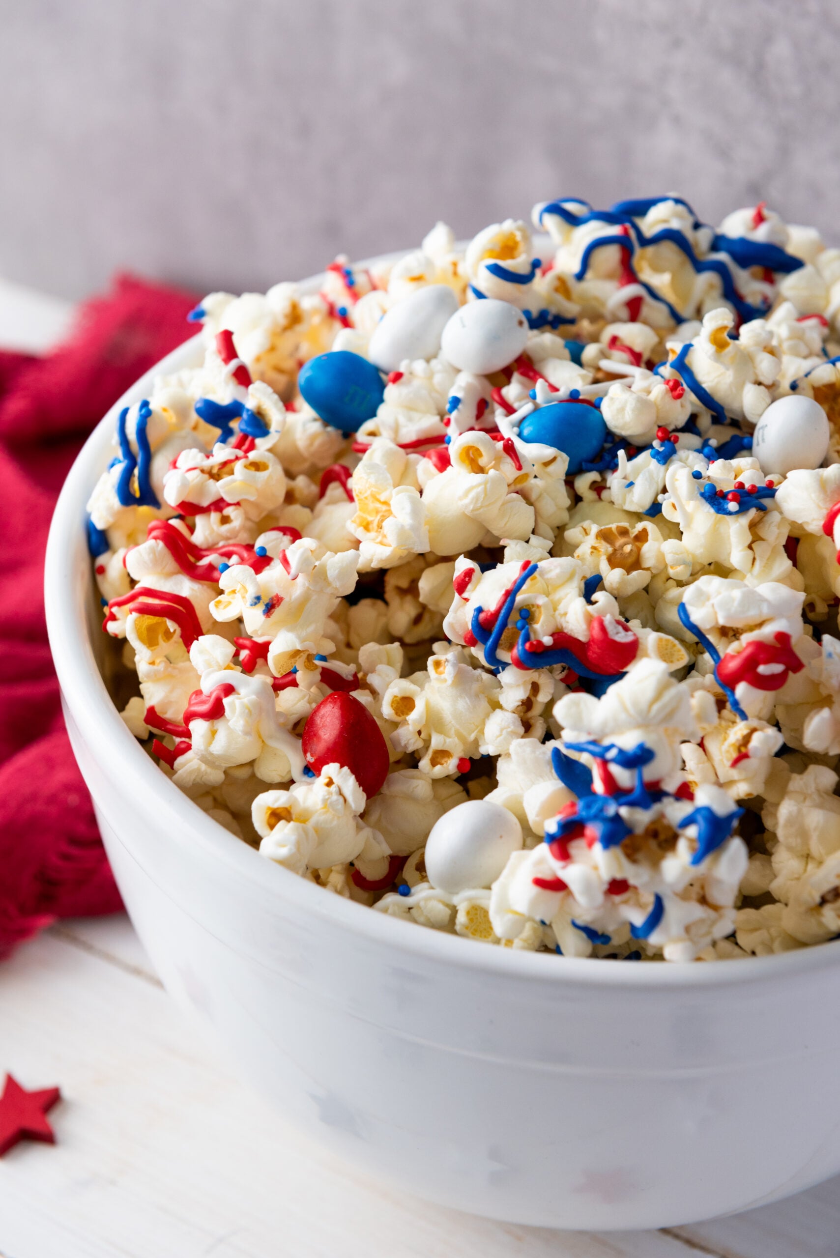 Red white and blue popcorn with chocolate candy in a white bowl.