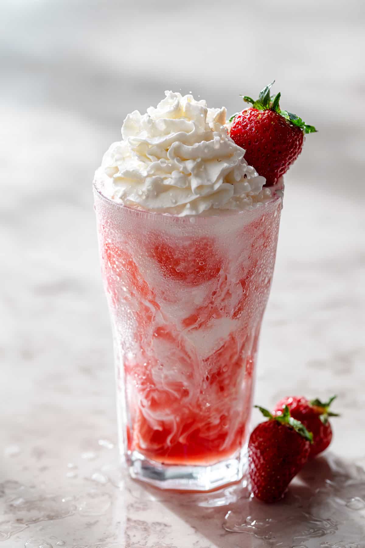 strawberry dirty soda with dr pepper on a marble background with a strawberry garnish