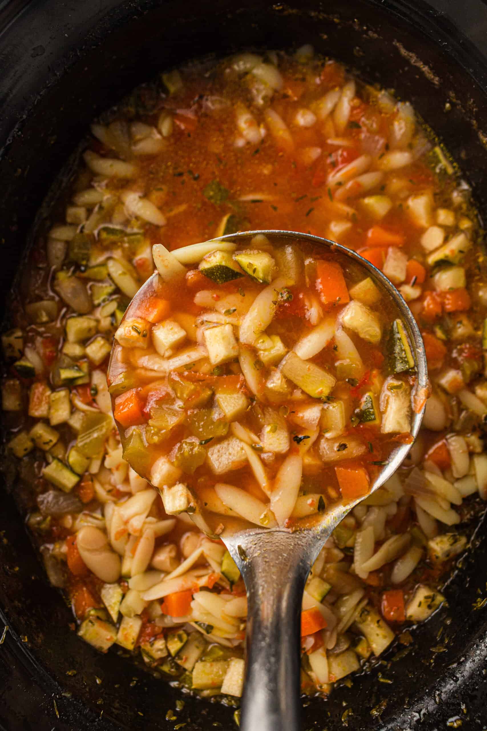 minestrone soup in a slow cooker with a scoop on a ladel