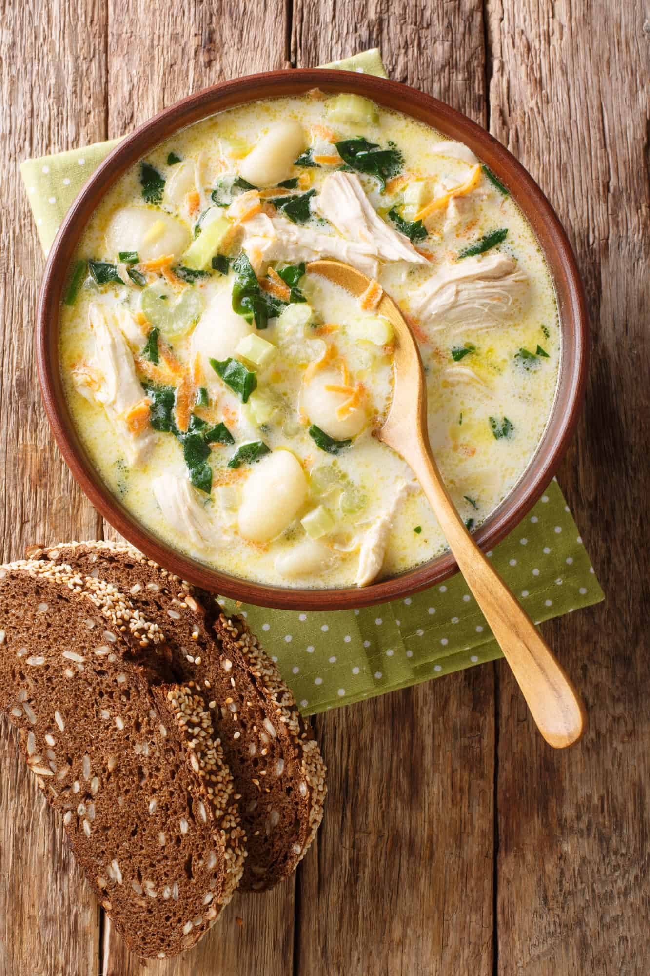 chicken gnocci soup in a brown bowl with a wooden spoon after cooking in a slow cooker