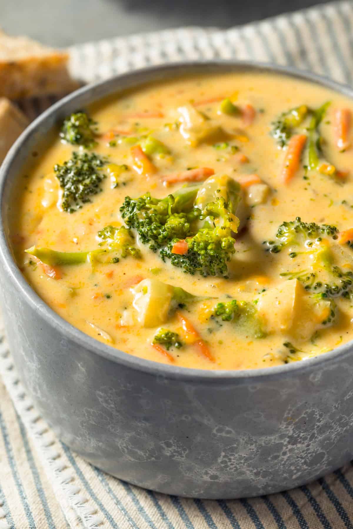 crock pot broccoli cheddar soup in a blue bowl with carrots