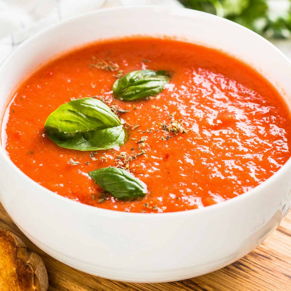 slow cooker tomato basil soup in a white bowl topped with fresh basil leaves is cozy for fall
