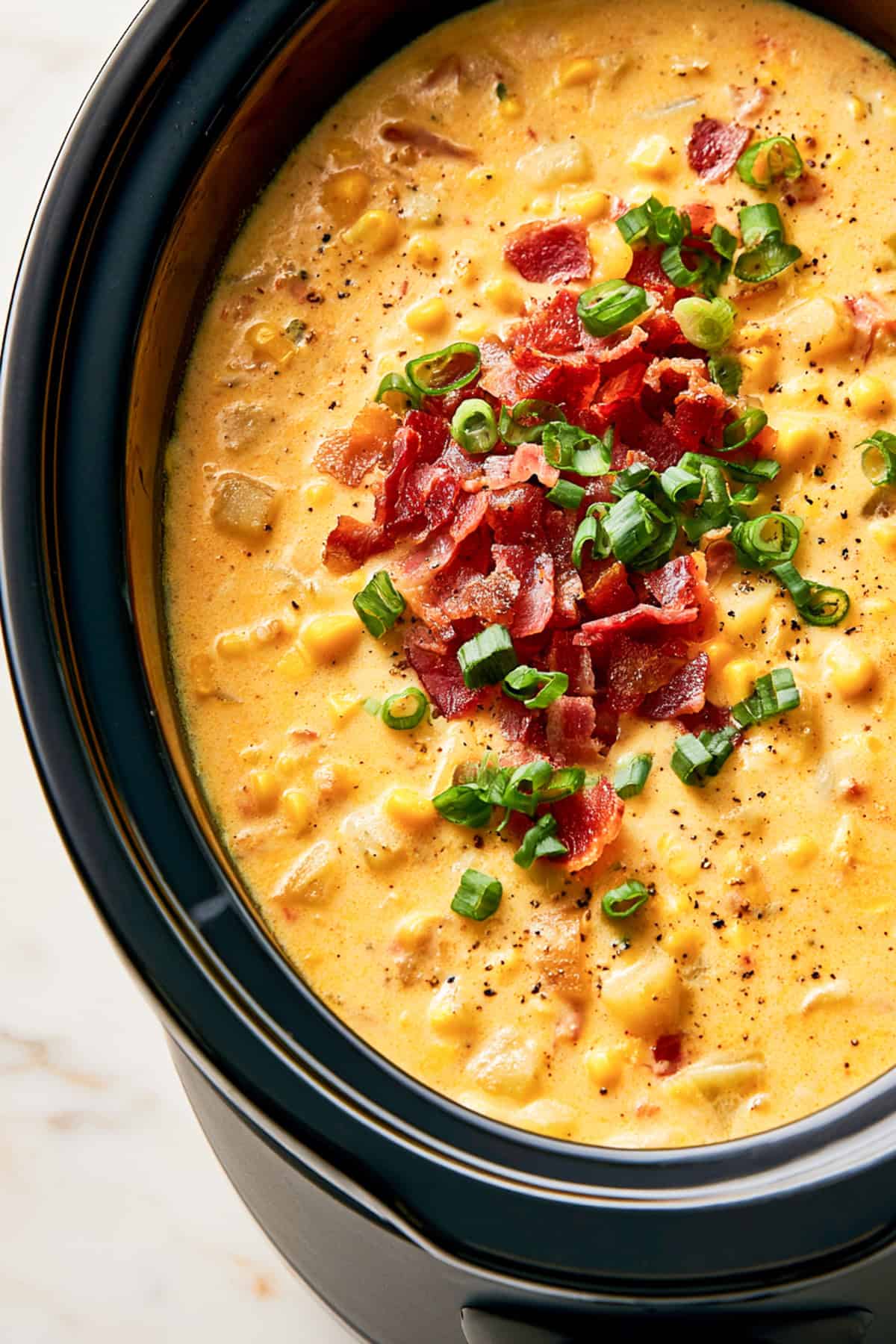 corn chowder topped with bacon in a black slow cooker