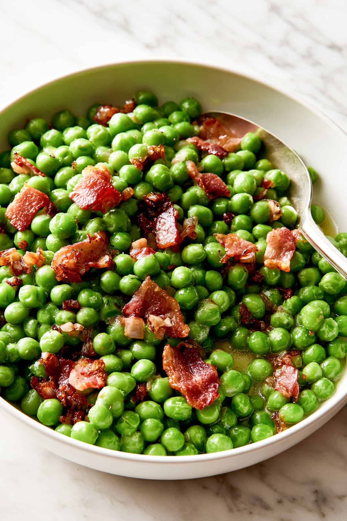 simple peas with bacon for thanksgiving in a white bowl with a spoon